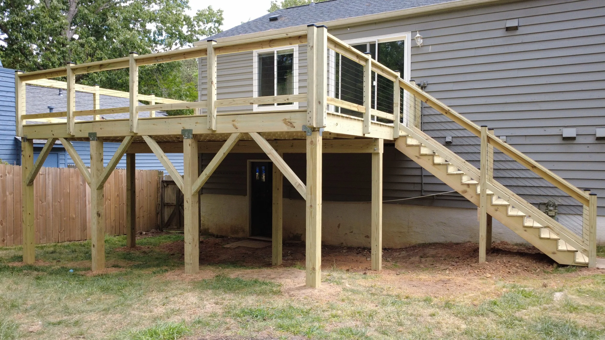 Newly built elevated wood deck with cable railing and a long staircase
